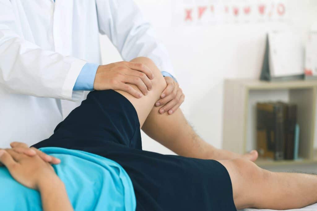 Arzt untersucht Knie eines Patienten im Liegen zur Diagnose von Gelenkbeschwerden.