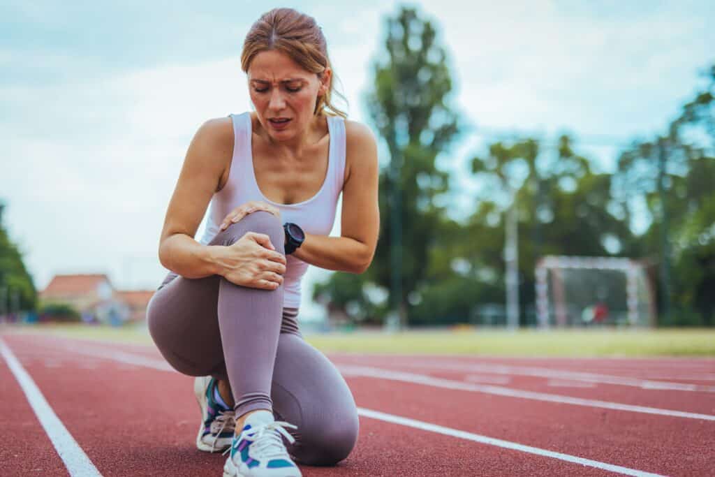 Sportlerin kniet auf Laufbahn und hält schmerzverzerrt ihr Knie – mögliche Sportverletzung oder Überlastung.